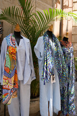 Fototapeta premium Colorful fashion display featuring vibrant dresses and scarves on mannequins with tropical plants in the background