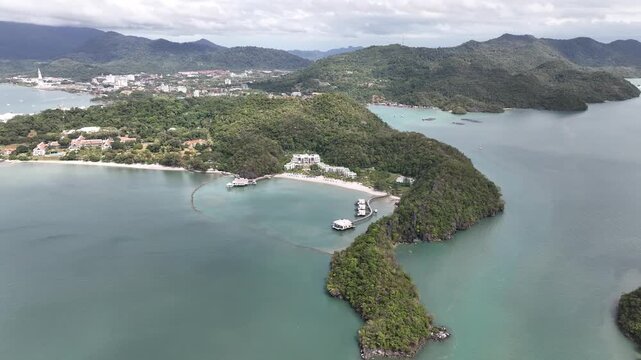High-Altitude Drone Fly Back and Pan Right Along Pantai Cenang Coastline Revealing Langkawi Resort, Channel, and Island Views on Sunny Cloudy Day