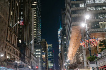 Multiple American flags line the street between tall Midtown skyscrapers glowing under the night...