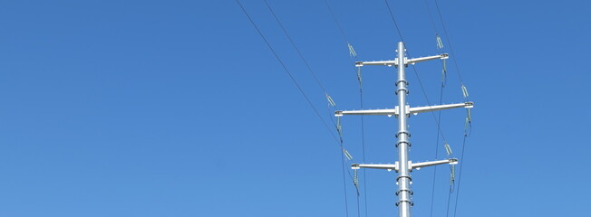 Tall utility pole with power lines against a clear blue sky, highlighting infrastructure and...