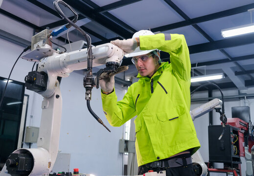 Worker maintains robotic arm in modern manufacturing facility during daytime hours for efficient production
