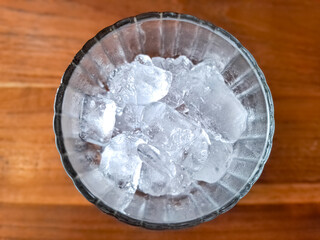 A glass full of ice cubes stands on a wooden table, top view