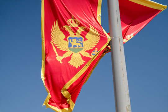 "montenegro's vibrant red and gold flag featuring the double-headed eagle flutters against a clear blue sky, symbolizing national pride and heritage on a sunny day."