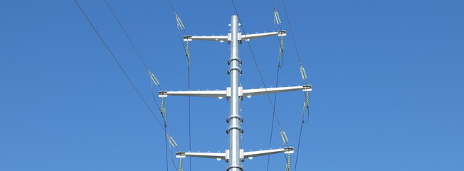 Metal utility pole with power lines against a clear blue sky, showcasing modern energy infrastructure and clean design.