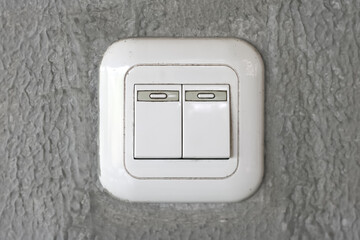 A white double light switch is mounted on a textured grey wall.