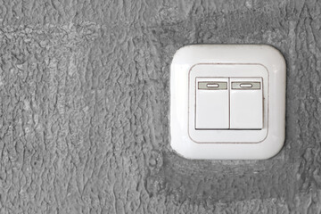 A white double light switch is mounted on a textured grey wall.