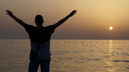 Rare of view man with raised hands at beach sunset