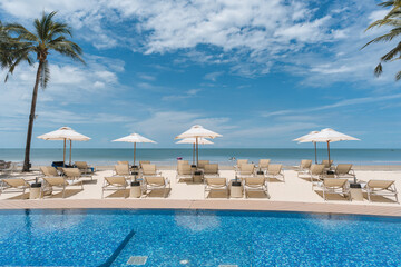 Beachfront resort with poolside, lounge chairs and white parasol on sunny day