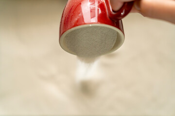 Flour pouring from red ceramic mug onto flat surface. Close-up food preparation process. Cooking,...