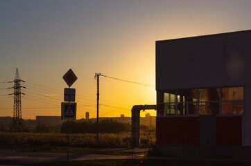 Obraz premium A road sign and other infrastructure in the light of the setting sun
