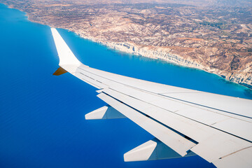 An airplane wing seen from a window. The plane flies over the holiday island of Cyprus.