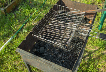 An overhead view of a metal charcoal grill and grill grate against a backdrop of green grass