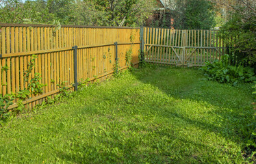 Rear inside corner of a new wooden staked fence in a garden with green grass. Parking area in the countryside