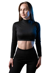A young healthy girl in a sports top and leggings poses in the studio against a black background.