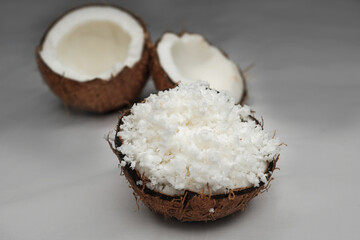 Freshly grated coconut pulp in cracked coconut shell and half of split coconut on white background. File contains clipping path.