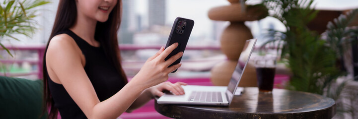 Asian adult woman works remotely modern business using laptop smartphone urban rooftop city view digital nomad professional connectivity