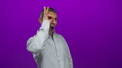 Man in striped shirt posing playfully with okay gesture against vibrant purple background, showcasing a confident and cheerful expression.