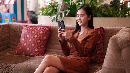 Fototapeta premium Asian adult woman uses smartphone connects online network for business communication social interaction digital lifestyle in modern hotel lobby lounge workspace