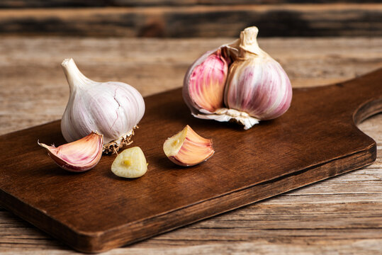 Garlic bulbs and cloves on a wooden cutting board, with a garlic clove split in half. Close-up.
