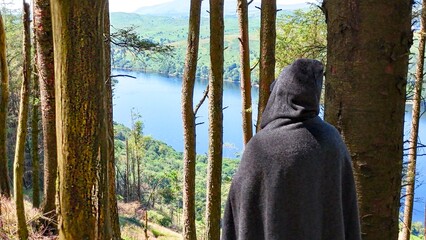 Mysterious cloaked character watches a lake from the shadows of woodland. Ideal for dark fantasy concepts © PJSCreativeWorks