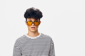 Young man wearing yellow sunglasses and black-and-white striped shirt with curly hair standing...