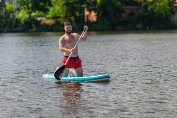 On a lake, a man of 30 years is floating on a SUP board.
