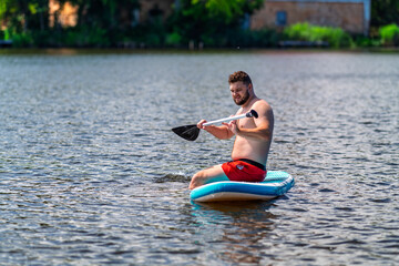 An young man is attempting to use a SUP board.