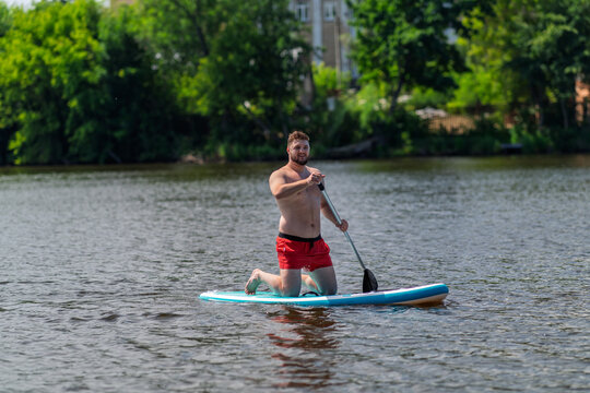 A 30 year old guy is floating on a SUP board on a lake.