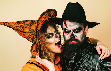 Halloween couple with pumpkin and Halloween makeup. Man and woman in witch hat celebrating...
