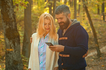 Autumn couple with phone. Happy couple using smart phone. Man typing write message on smart phone in autumn park. Social media. Business couple, man and woman with mobile phone on Autumn fall leaves.