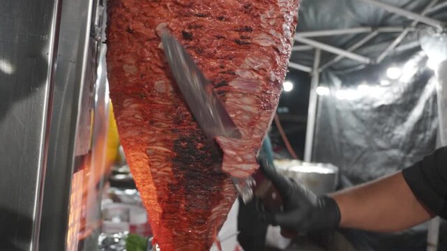 Street vendor Mexican taquero trompo al pastor,  cutting and serving up kebab style street foods 