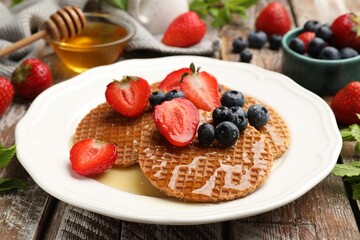 Tasty Dutch waffles (stroopwafels) with honey, strawberries and blueberries on wooden table, closeup