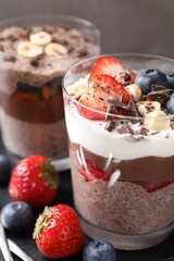 Delicious chocolate puddings with chia seeds, nuts and berries in glasses on table, closeup