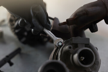 Auto parts. Professional mechanic with wrench fixing turbocharger at grey table indoors, closeup