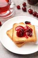 Toasts with tasty cherry jam, tea and fresh fruits on grey table , closeup