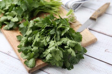 Cutting board with fresh cilantro and knife on white wooden table, closeup