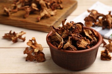 Dried chanterelle mushrooms in bowl on light wooden table, closeup