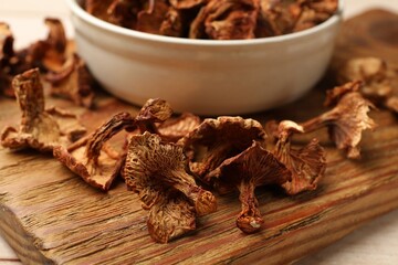 Dried chanterelle mushrooms in bowl on light wooden table, closeup