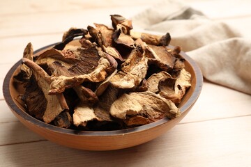 Pieces of dried mushrooms in bowl on light wooden table, closeup