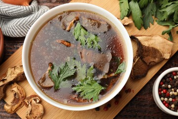 Tasty soup with mushrooms and parsley in bowl on wooden table, flat lay
