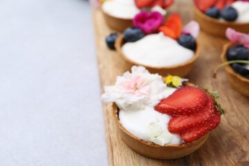 Sweet tartlets with berries and flowers on light table, closeup with space for text. Delicious dessert