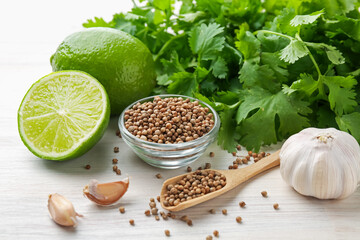 Coriander seeds, fresh cilantro, lime and garlic on light wooden table, closeup