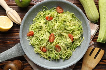 Tasty zucchini noodles with tomatoes, thyme and ingredients on wooden table, flat lay