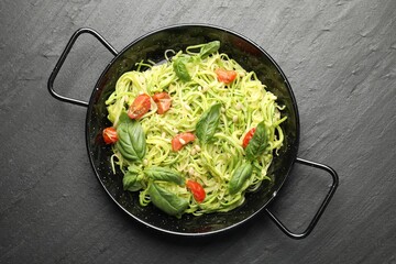Tasty zucchini noodles with tomatoes, pine nuts and basil on black table, top view