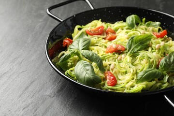 Tasty zucchini noodles with tomatoes, pine nuts and basil on black table, closeup