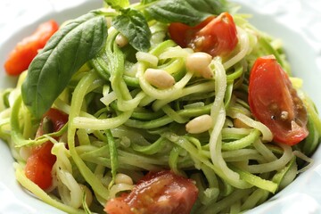 Tasty zucchini noodles with tomatoes, pine nuts and basil, closeup