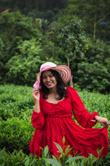 A woman in a stylish sunhat and red dress enjoys a serene moment in a lush tea plantation, surrounded by rolling green hills and nature.

