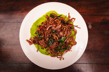 Top view of spicy Kerala-style prawns sautéed with caramelized onions and curry leaves, served on a banana leaf placed on a white plate, showcasing South Indian seafood cuisine.