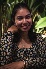 Confident Indian woman smiling while seated in tropical outdoor setting

