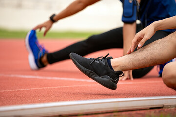 Close-up of two male athletes stretching legs on red running track focusing on sneakers and posture